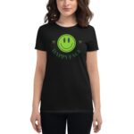 A woman wears a black t-shirt featuring a large green smiley face and the text HAPPY FACE above it while standing in an undefined indoor environment.