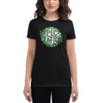 A woman is wearing a black t-shirt featuring the word "EXPECTATION" in a stylized font surrounded by green clovers  set against a neutral background.