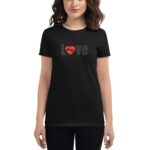 A woman is wearing a black t-shirt featuring the word Love in gray with a red heart and hands graphic display on the front  posed against a neutral background.