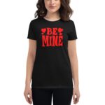 A woman wears a black t-shirt with bold red text reading BE MINE surrounded by small hearts showcasing a playful and romantic theme in a casual setting.