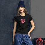 A young woman stands against a textured dark wall wearing a black t-shirt with a pink rose design and the word love beneath it  paired with blue jeans and a beanie.
