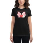 A woman wears a black shirt featuring a colorful graphic of gnomes holding a heart with the word "LOVE" surrounded by text that reads "A love like gnome other"