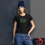 A young woman wearing a black t-shirt with green text stands against a textured backdrop. She has long hair and a beanie  presenting a casual style with light denim pants. The shirt features the phrase "make st. Patrick's Day great again."