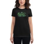 A person stands wearing a black t-shirt featuring festive green text and shamrocks that read "Happy St. Patrick's Day" in a casual setting.