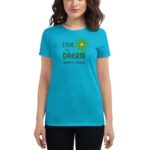 A person wearing a turquoise t-shirt displays the text "LIVE THE DREAM" with a flower graphic and "HAPPY ST. PATRICK" below  celebrating St. Patrick's Day in a casual setting.
