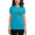 A woman wearing a bright turquoise t-shirt stands confidently. The shirt features the repeated phrase "LUCKY WOMAN" in various colors and styles  conveying a spirited message of positivity.