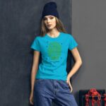 A woman in a bright blue t-shirt with a green text design stands confidently against a gray background wearing a navy beanie and relaxed denim jeans.