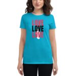 A woman wears a bright turquoise t-shirt featuring the word "LOVE" in large red and black letters repeatedly  standing against a plain background.