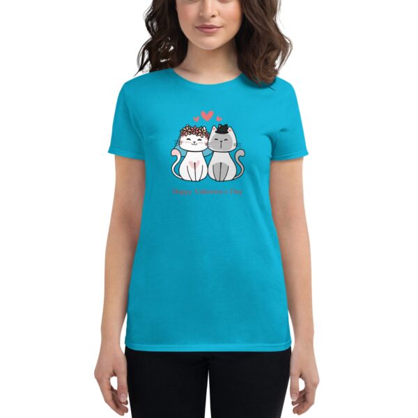 A woman wears a bright turquoise t-shirt featuring a cartoon design of two cats  one with a floral crown and the other with a bow tie  expressing a Valentine's Day theme underneath.