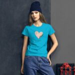 A young woman stands against a dark wall wearing a bright blue t-shirt featuring a heart design and the text Happy Valentine's Day while dressed in casual denim and a dark beanie.