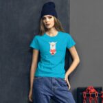 A young woman stands against a textured gray wall wearing a bright turquoise t-shirt featuring a cartoon llama holding a heart with the text Happy Valentine's Day and casual denim jeans.