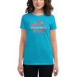 A young woman wears a bright turquoise t-shirt with the text Happy Valentine's Day surrounded by floral designs against a plain background suggesting a festive and cheerful atmosphere.