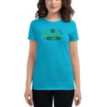A woman is wearing a bright turquoise t-shirt featuring green St Patrick's Day themed text and a shamrock design in a neutral background environment.