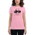 A woman is wearing a pink t-shirt featuring a smiling face with black sunglasses and the text LUCKY DAY with a small green leaf underneath in a casual setting.