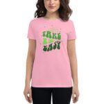A person wears a pink t-shirt featuring the phrase “TAKE IT EASY” in green and black stylized text with stars in the background  standing in a neutral setting.
