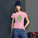 A young woman stands confidently wearing a pink t-shirt with green text that reads "Every journey needs a first step Happy St. Patricks 2024" against a dark textured background.