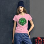 A young woman wears a pink t-shirt featuring a green St. Patrick's Day design while posing against a dark background with industrial elements and red chains nearby.
