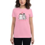 A woman wears a pink t-shirt featuring two cartoon cats  one with a flower crown and the other with a party hat  and the text "Happy Valentine's Day" below them.