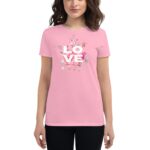 A woman is wearing a pink t-shirt featuring the word LOVE in white  surrounded by floral designs  while standing in a neutral setting with minimal distractions.