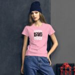 A young woman leans against a dark wall wearing a pink shirt with the text "HAPPY LOVE DAY" while sporting a blue knit beanie and casual jeans.