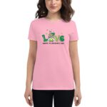 A woman wearing a pink t-shirt with the word "Love" and a graphic featuring a hat and clovers celebrates St. Patrick's Day in a casual indoor setting. Text reads "HAPPY ST.PATRICK'S DAY."