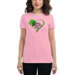 A woman is wearing a pink shirt featuring a green heart design with the text Happy St. Patrick's Day and a shamrock  standing against a neutral background.