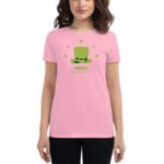 A woman is wearing a pink t-shirt featuring a green leprechaun hat graphic with text that reads CHEERS HAPPY ST PATRICKS DAY surrounded by small green shamrocks in a casual setting.