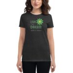 A person wears a black t-shirt featuring a green flower graphic with the text "LIVE THE DREAM" above and "HAPPY ST. PATRICK" below in green and white.