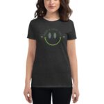 A person wears a dark-colored t-shirt featuring a large smiley face design with the text "HAVE A LUCKY DAY" above it  set against a neutral background.