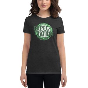 A woman stands wearing a black t-shirt with the word EXPECTATION in green surrounded by a circular pattern of green leaves in a casual indoor setting.