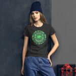 A young woman wears a dark t-shirt with a festive St. Patrick's Day design featuring clovers and a heart. She stands against a textured gray background with a chain and boxes nearby.