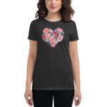 A woman stands wearing a black t-shirt adorned with a floral heart design featuring pink and blue flowers against a neutral background  presenting a casual and vibrant look.