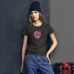 A young woman stands against a gray wall wearing a black t-shirt with a pink rose design and the word love while dressed in blue jeans and a blue beanie.