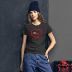 A young woman wearing a dark t-shirt with a red heart graphic stands against a dark wall. She has long hair and a blue knit beanie  exuding a casual style.