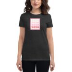 A woman stands wearing a dark t-shirt featuring a graphic design of a stamp with the word "XOXO" in various colors  set against a neutral backdrop.
