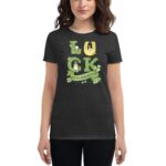 A woman wears a dark gray t-shirt featuring the word "LUCK" with decorative elements like a horseshoe and shamrocks celebrating St. Patrick's Day  set against an informal backdrop.