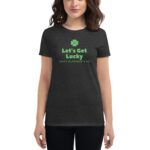 A woman is wearing a black t-shirt featuring green text and a clover symbol The text reads Let's Get Lucky and Happy St Patrick's Day