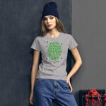 A young woman stands confidently wearing a grey t-shirt with green text celebrating St. Patrick’s Day her dark knit hat contrasts with the background of dark gray and chains. Text reads: EVERY JOURNEY NEEDS A FIRST STEP HAPPY ST. PATRICKS 2021