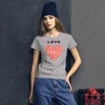 A young woman wears a gray t-shirt with a red heart design and the word "LOVE" above it while standing against a dark wall with a box and red chains nearby.