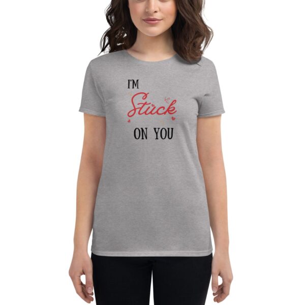 A woman wears a grey t-shirt with the text I'm Stuck on You displayed in a playful font along with decorative hearts  standing against a neutral background.