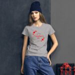 A young woman stands confidently wearing a grey t-shirt with "Happy Valentine's Day" text and red hearts  complemented by a navy beanie  against a dark textured background.