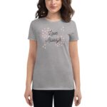 A gray t-shirt with the words Love Always printed in a cursive font surrounded by pink circles and sparkles is worn by a woman standing against a plain background.