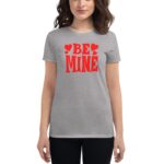A woman is wearing a light grey t-shirt featuring bold red text that says BE MINE with hearts. She stands against a plain background.