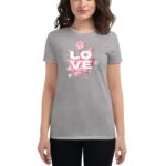 A woman is wearing a grey t-shirt featuring the word "LOVE" in bold white letters alongside pink floral designs  standing with her arms relaxed at her sides against a neutral background.