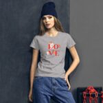 A young woman stands confidently wearing a gray t-shirt with a colorful "LOVE" graphic and denim jeans against a dark background featuring a red chain and a box.