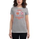 A gray t-shirt features cartoonish heart characters celebrating love with cheerful expressions holding flowers and hearts surrounded by text that says HAPPY VALENTINE'S DAY in colorful letters