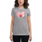 A woman stands wearing a gray t-shirt featuring a colorful graphic of gnomes holding a heart. The text above reads A love like gnome other. The setting is casual.