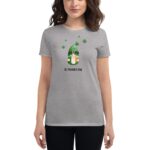 A woman is wearing a gray t-shirt featuring a whimsical gnome design with a green hat and a message reading St. Patrick's Day surrounded by shamrocks in a casual indoor setting.