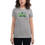 A woman is wearing a grey t-shirt with a festive green graphic reading "Happy St. Patrick's Day" alongside a shamrock  standing against a neutral background.