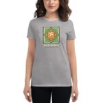 A woman wears a gray t-shirt featuring a colorful design with a shamrock that says HAPPY ST. PATRICK'S DAY  standing in a neutral background.
